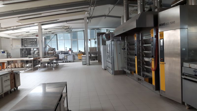 Blick in die große, leere Produktionshalle der Bäckerei. Man sieht viele Regale und Öfen.
