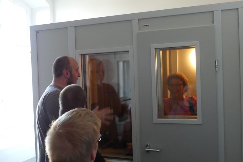 Brigitte ist in der Tonkabine. Bernd und andere Kellegen aus der AG sehen von außen hinein.