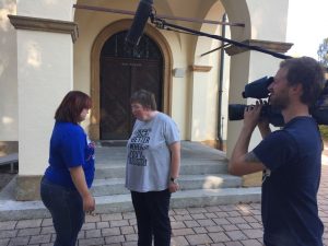Simone und Silvia stehen vor der evangelischen Kirche in Neukirchen und führen ein Interviewgespräch. Rechts vorne sieht man den Kameramann von OTV.