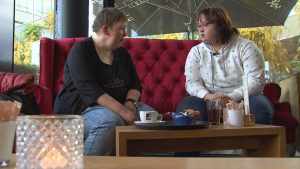 Silvia und Simone sitzen auf einem gemütlichen roten Sofa in einem Cafe bei den Dreharbeiten.