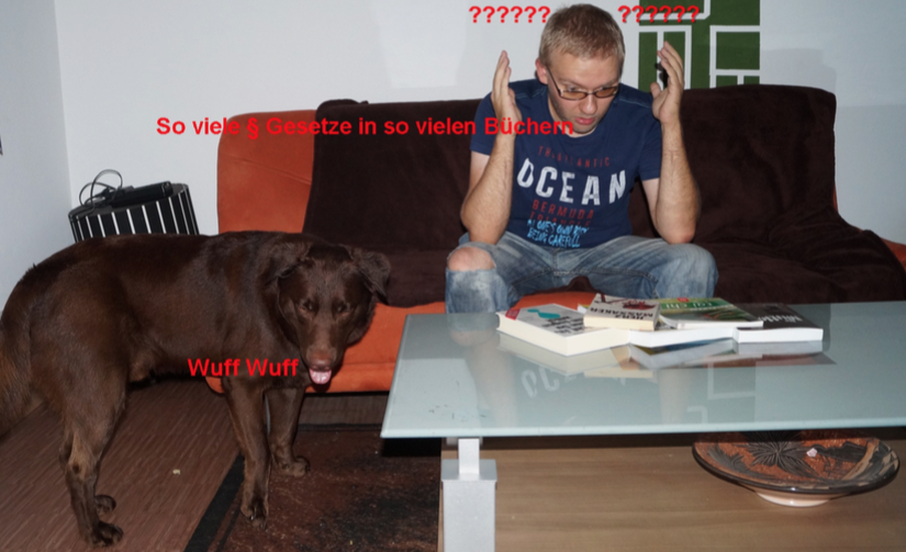 Andreas und Therapiehund Janosch vor einem Tisch auf dem Gesetzesbücher liegen. Andreas sieht verzweifelt aus.