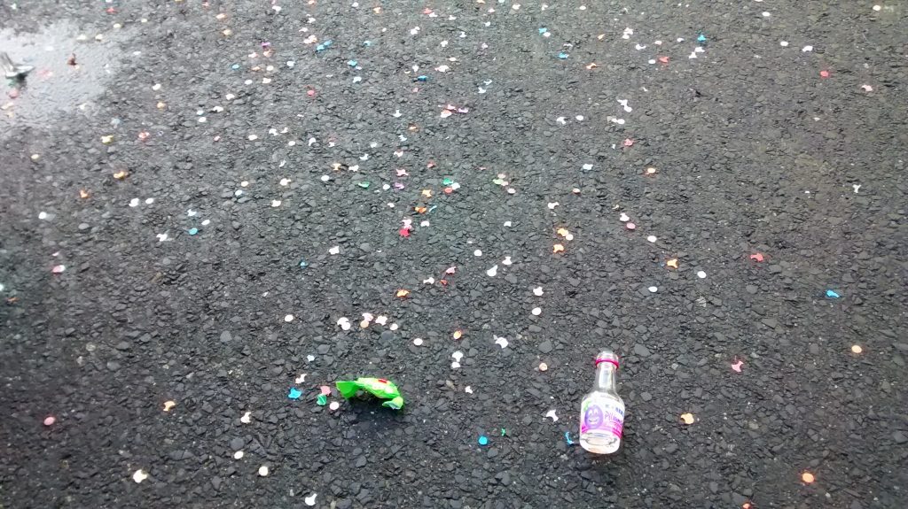 Eine kleine Schnapsflasche und Konfetti liegen auf der Straße