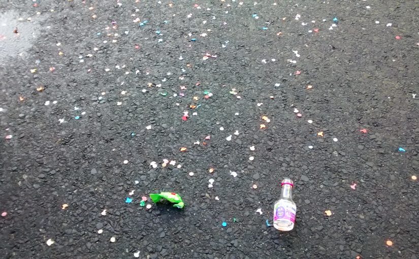 Eine kleine Schnapsflasche und Konfetti liegen auf der Straße