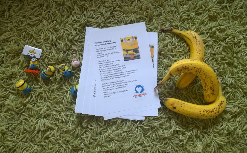 Einladungsflyer für den Kinotag liegen auf einem Teppich. Daneben sind kleine Minions-Figuren und drei Bananen.