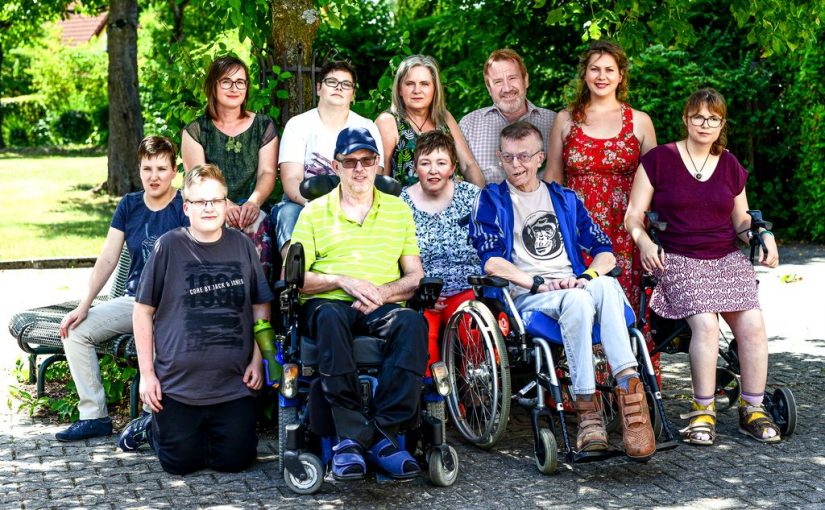 Gruppenbild mit allen Teilnehmer/innen beim Fotoshooting auf einer Bank unter einem Baum im hellen Sonnenlicht