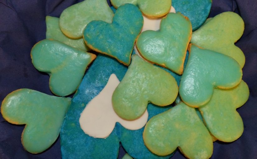 Auf dem Foto sind Plätzchen in Herzform zu sehen. Sie sind mit Zuckerguss in weiß, grün und blau verziert.