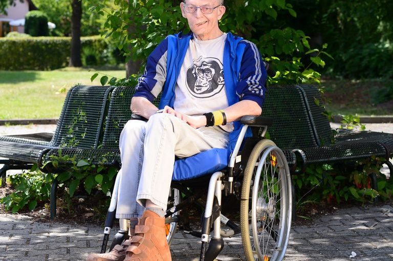 Werner sitzt im Rollstuhl im Grünen und lächelt in die Kamera.