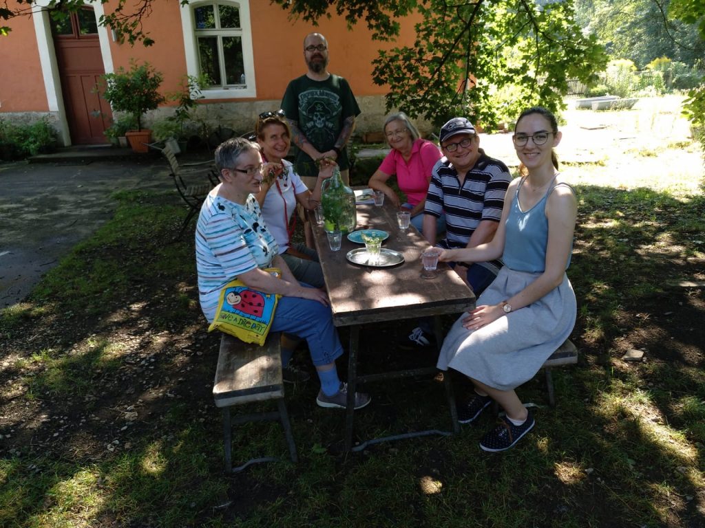 Unser Drehteam sitzt gemeinsam mit Frau Bräutigam an einem Holztisch im Grünen.