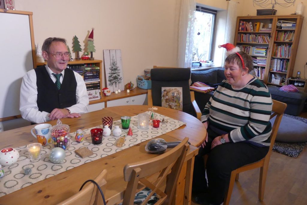 Auf dem Foto sitzen Josef Schmaußer und Silvia Stiegler an einem weihnachtlich geschmückten Tisch und bereiten sich auf das Interview vor. Beide lachen.